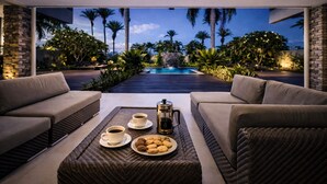 Un espace de détente extérieur moderne avec vue sur la piscine, comprenant un canapé, une table basse avec une tasse de café, une assiette de biscuits et une cafetière.