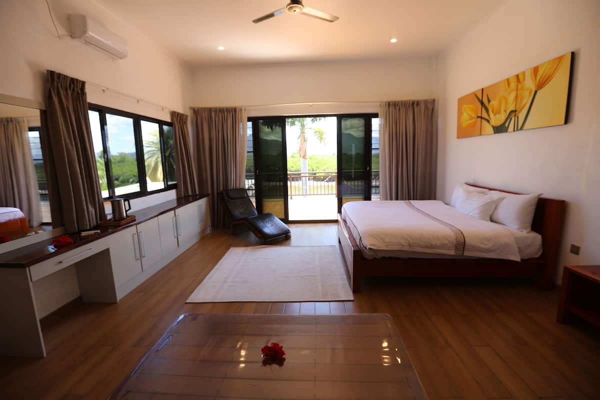 Ein Schlafzimmer mit Bett, Schreibtisch, Stuhl und Blick ins Freie durch eine Schiebetür.