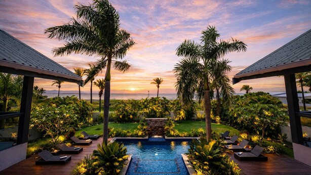 Un espace piscine doté de chaises longues, de palmiers et offrant une vue sur le coucher de soleil.