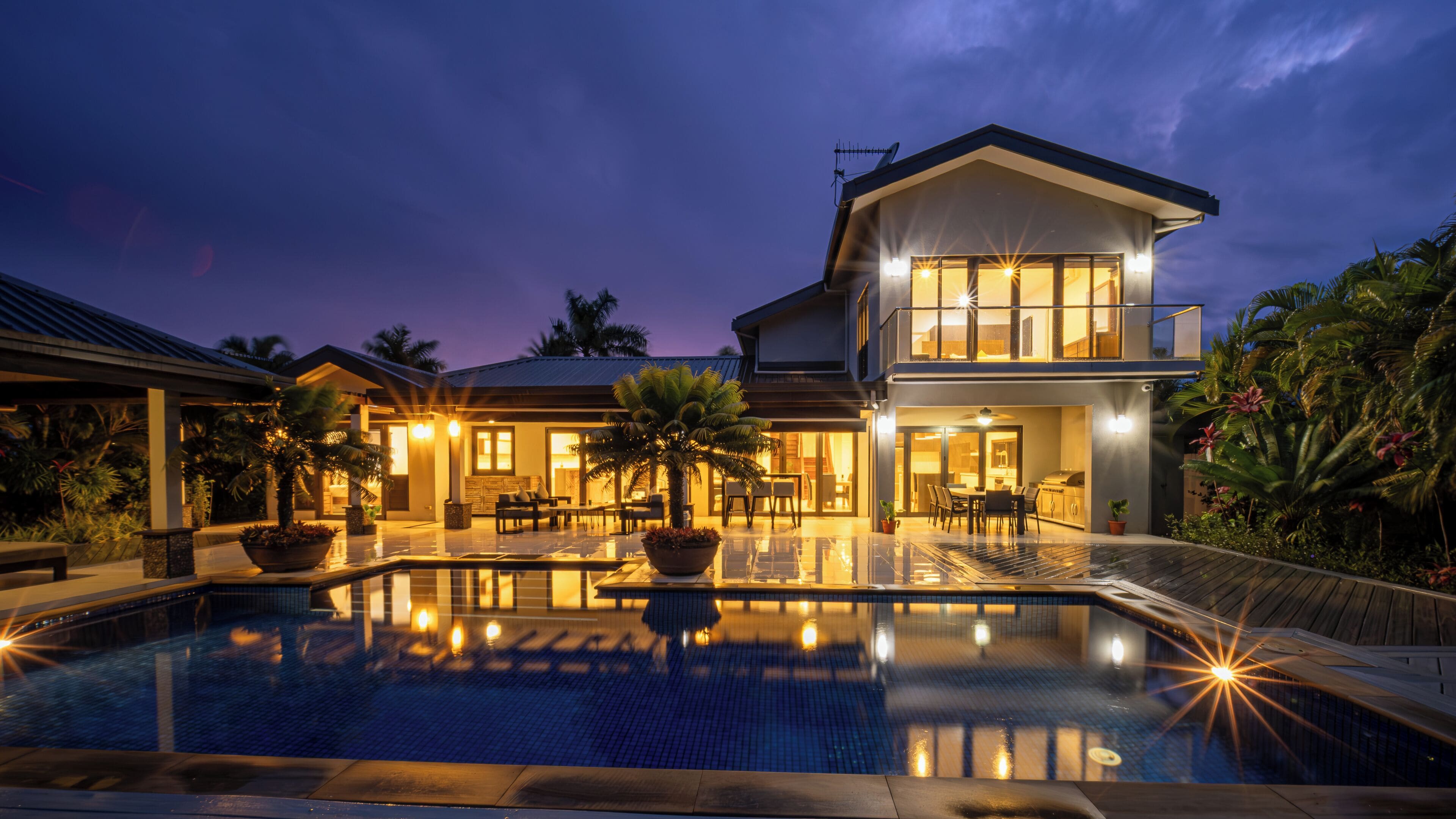 A two-story house with a swimming pool, outdoor seating, and a well-lit patio area.