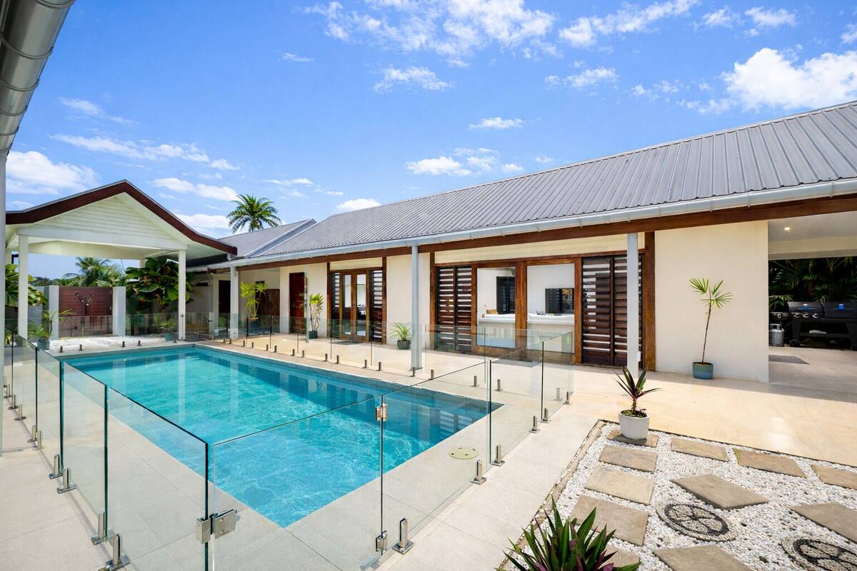 Ein moderner Poolbereich im Freien mit einem klaren, blauen Pool, einer überdachten Terrasse und einem Grillplatz.