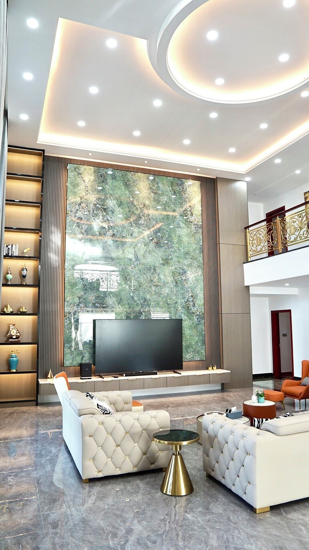 A modern living room with a large TV, comfortable seating, a bookshelf, and a large window with a view of greenery.