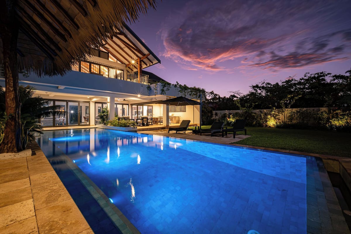 Ein modernes Haus mit Swimmingpool, Sitzgelegenheiten im Freien und einer gut beleuchteten Terrassenfläche.