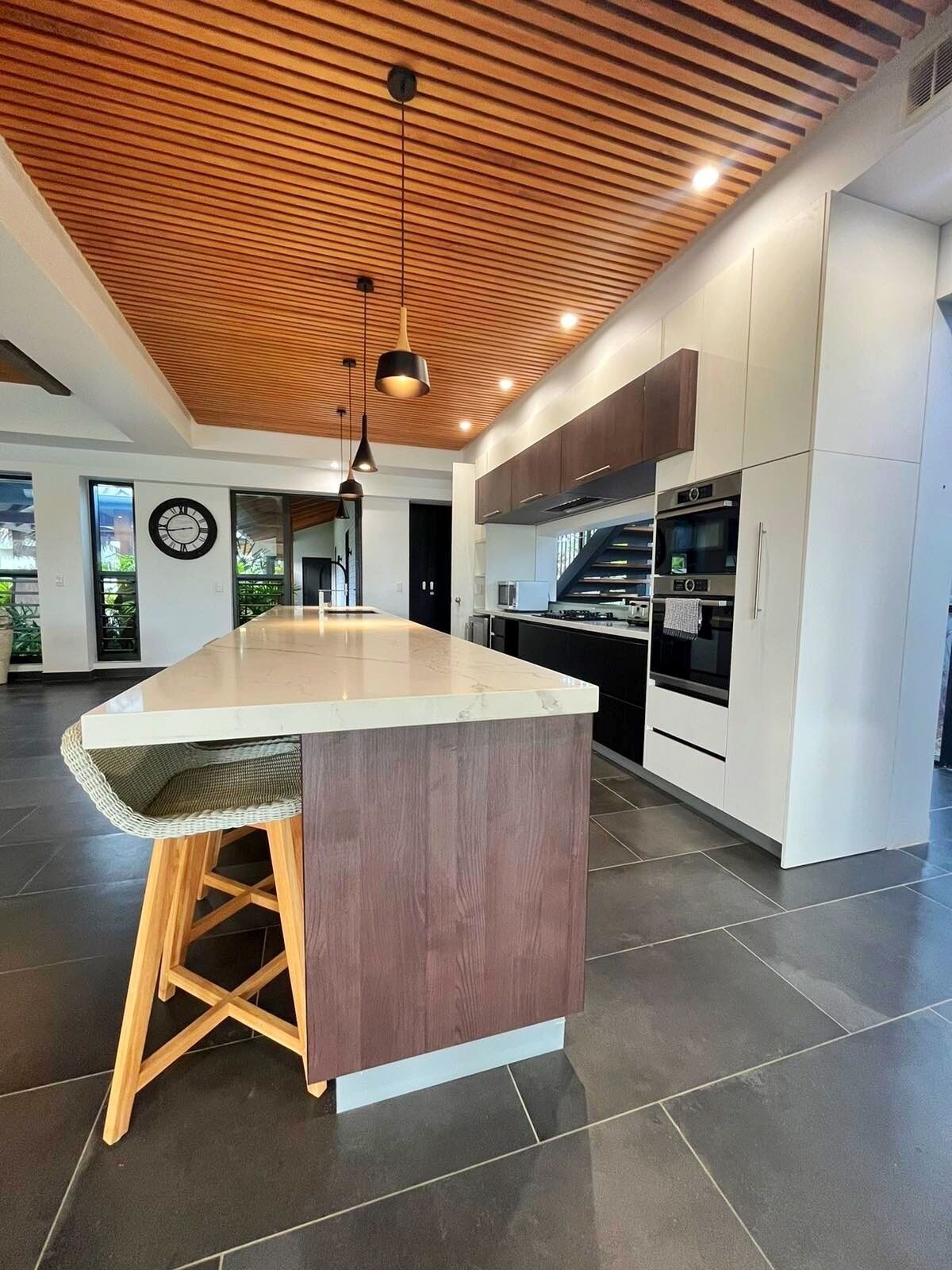 A modern kitchen with a large island, wooden ceiling, and built-in appliances.