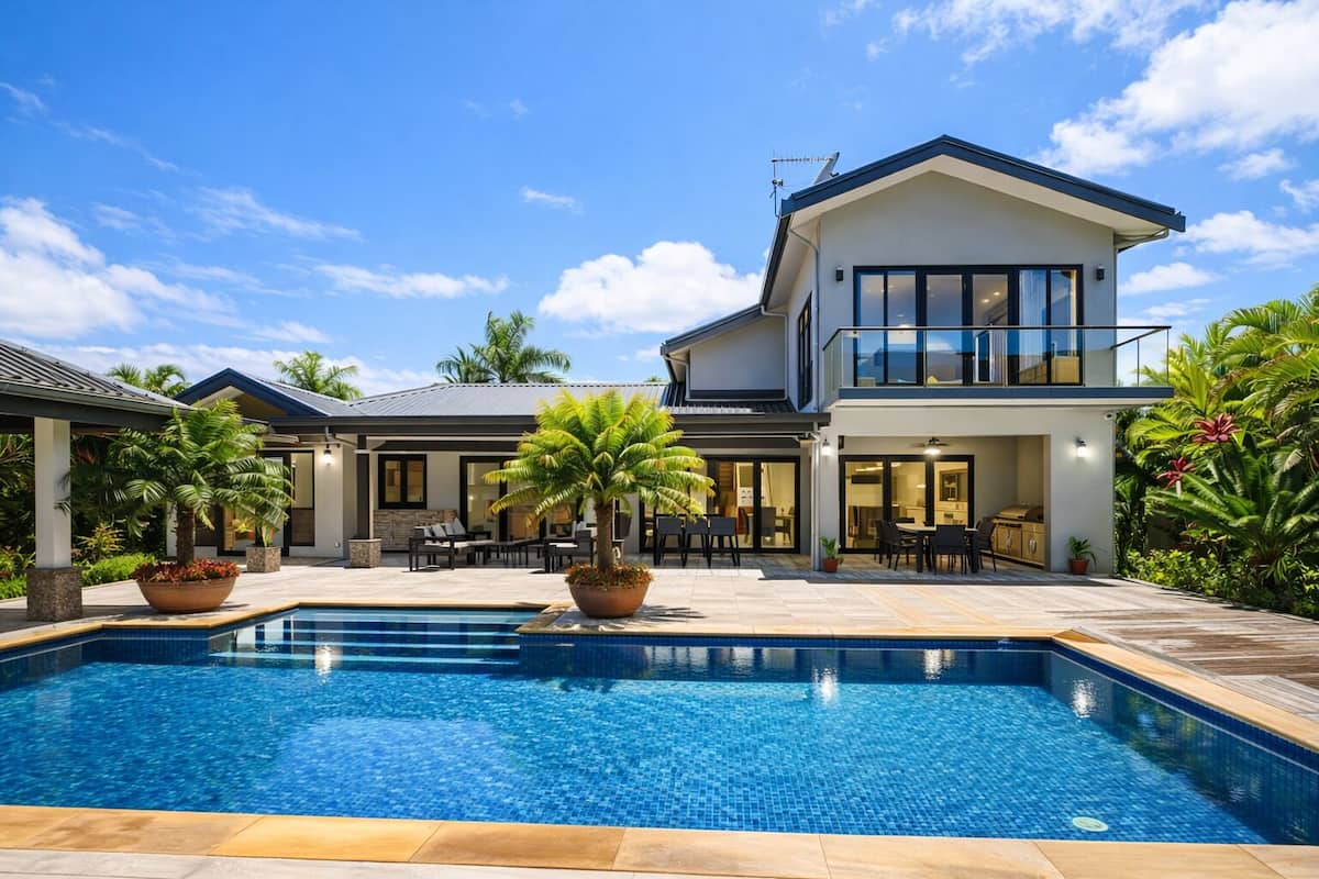 Ein modernes, zweistöckiges Haus mit Swimmingpool, Sitzgelegenheiten im Freien und üppiger Bepflanzung.
