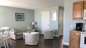 A living room with a sofa, two chairs, a coffee table, and a kitchen area with cabinets and appliances. - Atlantic Ocean Suites - Sand Castle Suite 7 (Old Orchard Beach)