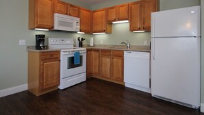 A kitchen with wooden cabinets, a white refrigerator, a microwave, a stove, and a dishwasher. - Atlantic Ocean Suites - Sand Castle Suite 7 (Old Orchard Beach)