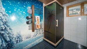 A bathroom with a snow-themed mural, a glass shower enclosure, and a window with a rural landscape view.
