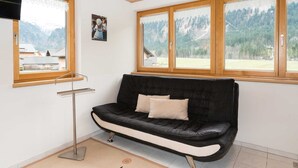 A room with a black leather sofa, a standing lamp, and large windows with a mountain view.