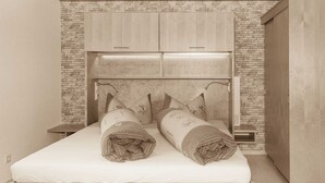 A bedroom with a wooden headboard, a brick accent wall, and a wooden wardrobe.