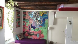 A room with a bed, a table, and a wall covered with colorful artwork.