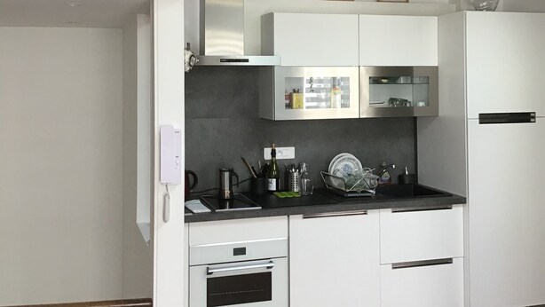 A kitchen with white cabinets, a stainless steel oven, and a black countertop. There are framed pictures on the wall above the cabinets.