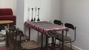 A dining area with a table, chairs, and a red sofa. There are framed pictures on the walls and a plant on the ceiling.