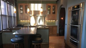 A modern kitchen with a central island, bar stools, stainless steel appliances, and wooden cabinets. - 9 Bedroom Historic Summit Mansion With Pool And Hot Tub (St Paul)