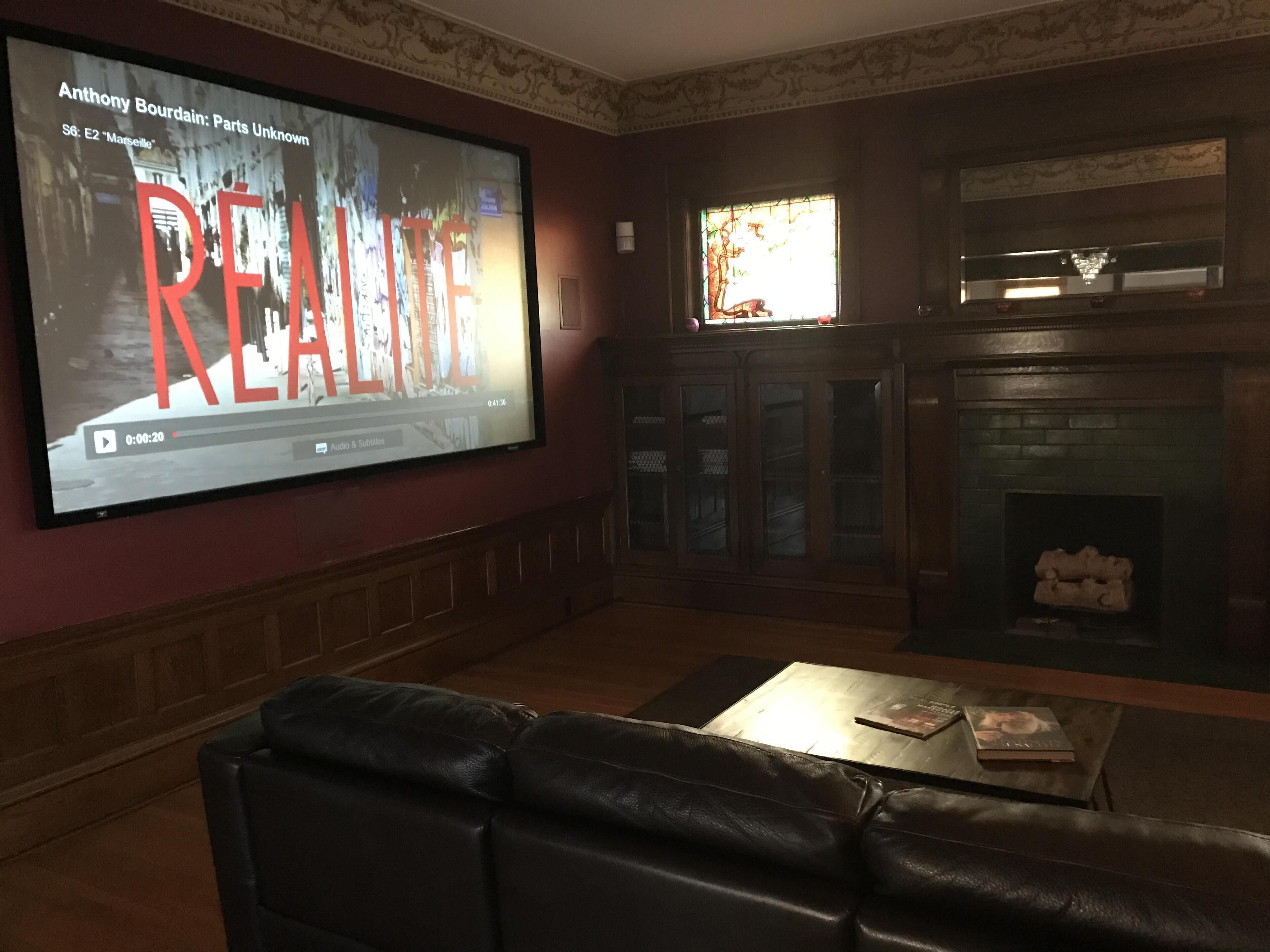 Una sala de estar con una amplia televisión de pantalla plana montada en la pared, chimenea y sofá de cuero.