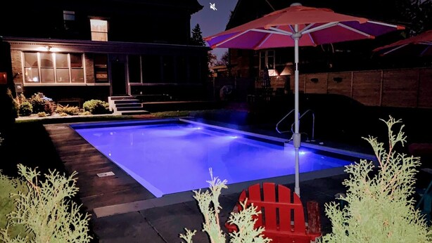 A swimming pool with a blue-lit edge, surrounded by a wooden deck and red chairs. - 9 Bedroom Historic Summit Mansion With Pool And Hot Tub (St Paul)