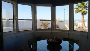 Un comedor con una mesa y sillas, un bol de pan y vista al mar a través de amplios ventanales.