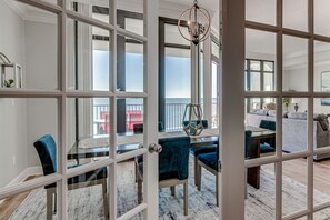 A spacious room with a large window, a dining area with blue chairs, and a chandelier. - Beach Front, Spacious, Clean and Comfortable (Orange Beach)