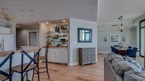 Een moderne keuken met witte kasten, een houten eiland, en een zithoek met blauwe stoelen en een grijze bank.