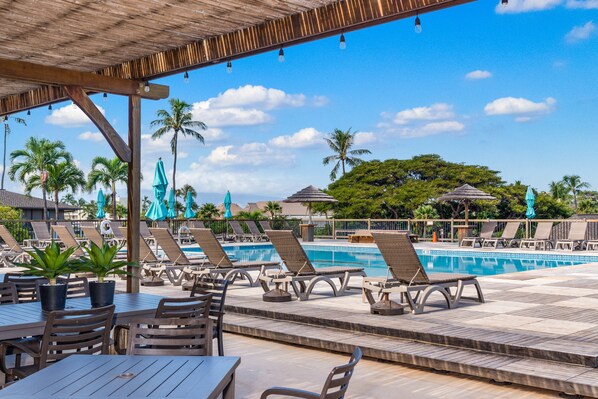A poolside area with lounge chairs, a pool, and a covered seating area.