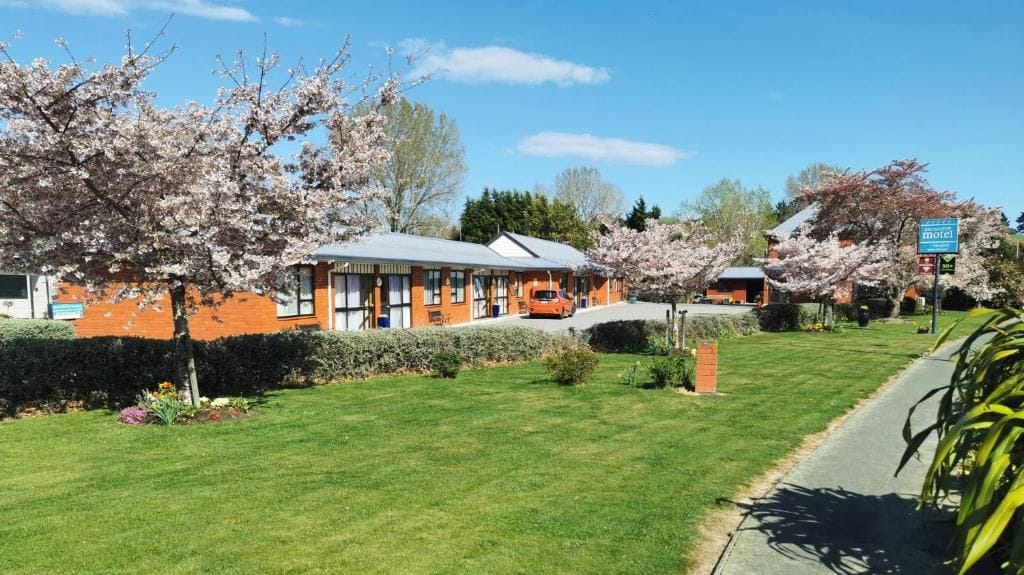 A motel with a single-story structure, a car parked in front, and cherry blossom trees in the background.