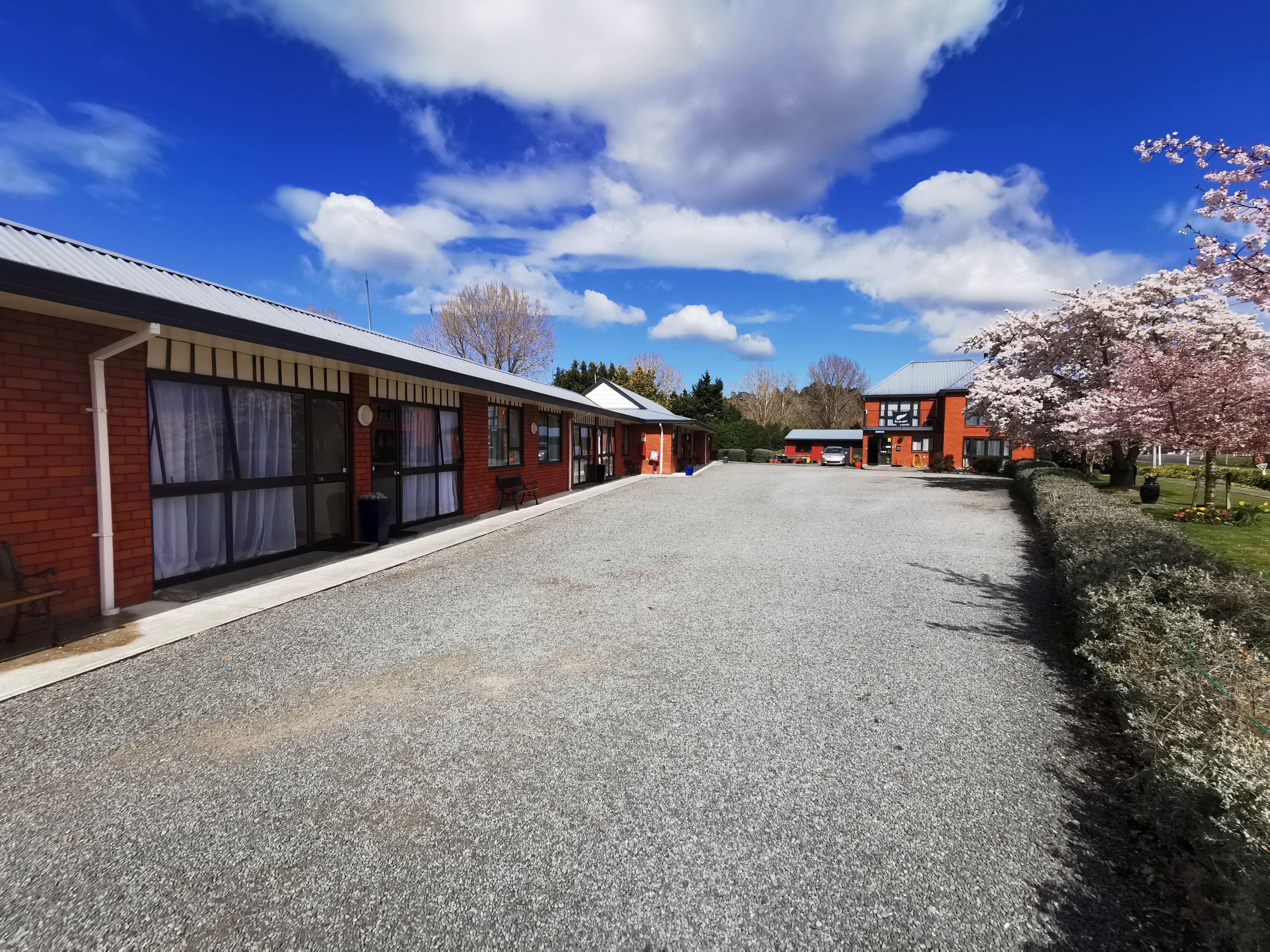 A hotel with a gravel driveway, brick buildings, and a cherry blossom tree.