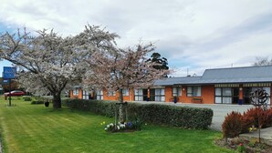 A building with a brick facade, a large tree with white blossoms, and a well-maintained lawn. - Broadview Motel (Cheviot)