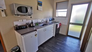 A compact kitchen with a microwave, stove, sink, and a small refrigerator. - Broadview Motel (Cheviot)