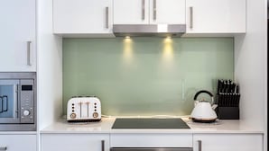 Une cuisine moderne avec des meubles blancs, une hotte en acier inoxydable, un grille-pain, une bouilloire et un bloc à couteaux.