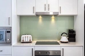 Eine moderne Küche mit weißen Schränken, einer Edelstahl-Dunstabzugshaube, einem Toaster, einem Wasserkocher und einem Messerblock.