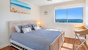 Une chambre à coucher avec un lit, une table de chevet, une lampe, une décoration en forme d’étoile et une fenêtre donnant sur la mer.
