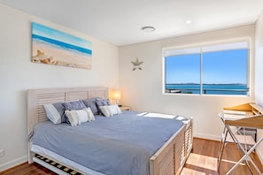 Een slaapkamer met een bed, nachtkastje, lamp, een ster decoratie en een raam met uitzicht op zee.