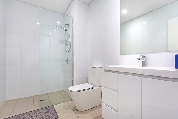 A modern bathroom with a glass shower enclosure, a white toilet, and a white vanity with a mirror.
