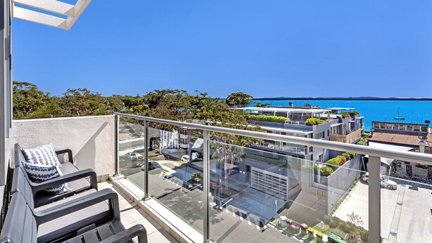 Un balcon doté d’une balustrade en verre, donnant sur un quartier résidentiel et un plan d’eau.