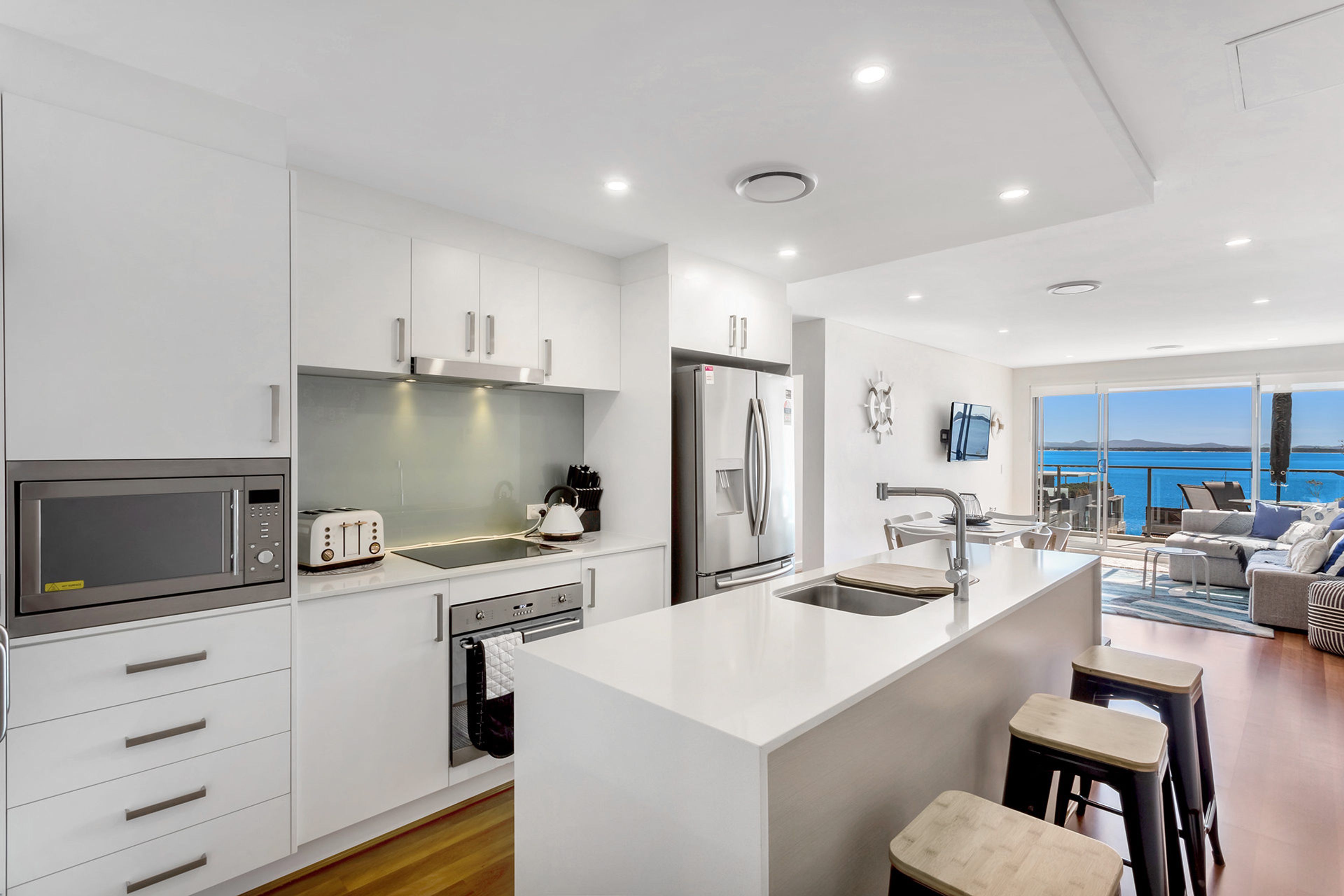 A modern kitchen with white cabinetry, stainless steel appliances, and a large island with bar stools.
