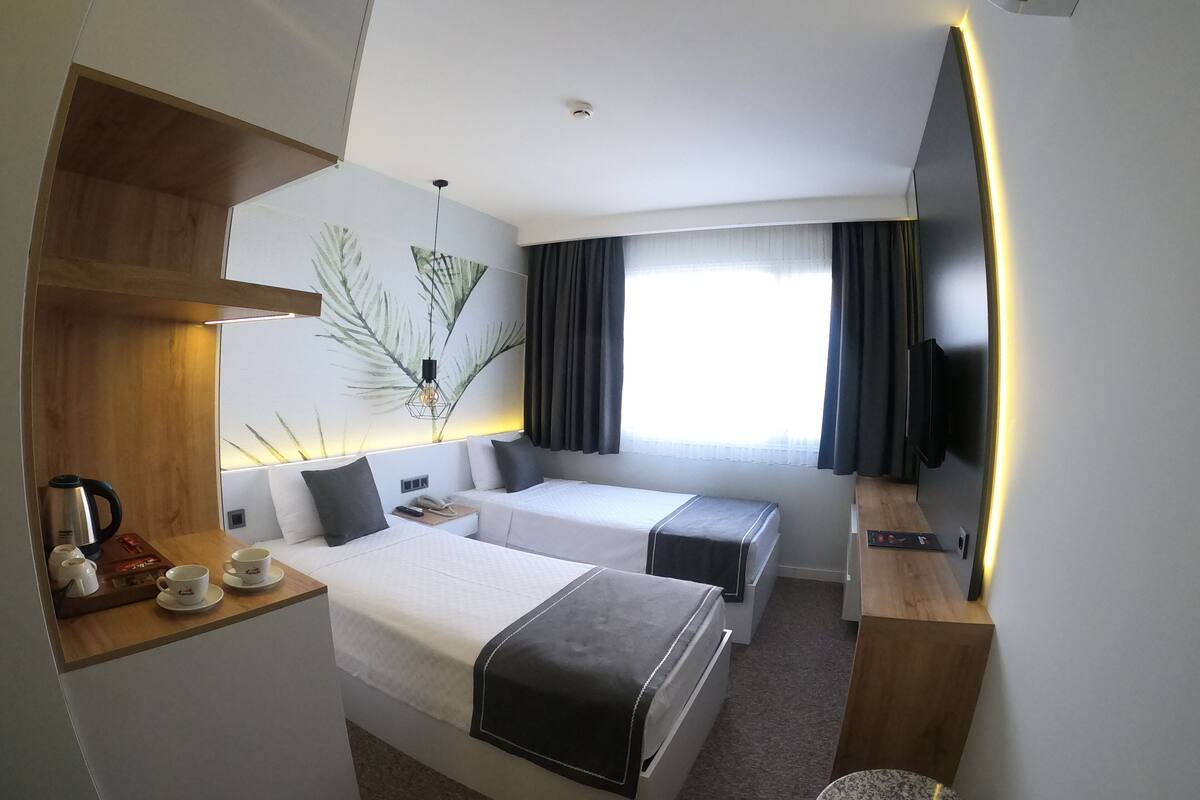 Een hotelkamer met twee bedden, een televisie, een koffiehoek en een groot raam met gordijnen.