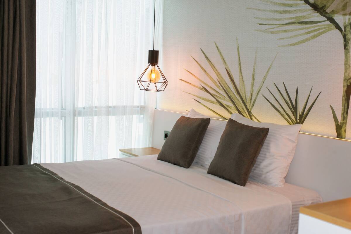 Een hotelkamer met een bed, een nachtkastje, een wandlamp en een grote potplant.