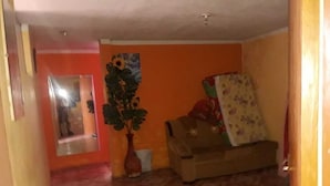 A room with a tiled floor, a sofa, a large potted plant, and a wall with a mirror and a painting. - Third floor apartment (Ayacucho)
