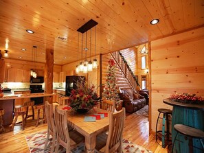 Interior de una cabaña de madera con comedor, cocina y una escalera.