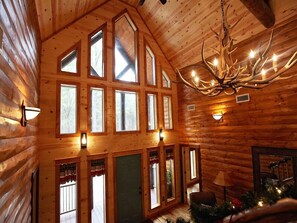 L’intérieur d’une cabane en rondins, avec de nombreuses fenêtres, un lustre et une cheminée.