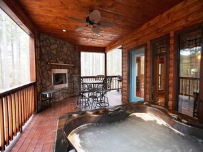 Una cabaña de madera con chimenea de piedra, jacuzzi y un patio con mobiliario exterior.