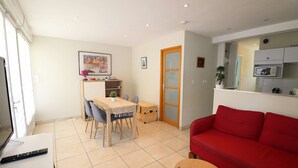 Un salon avec un canapé rouge, une table à manger en bois avec des chaises, une petite table ronde et un coin cuisine équipé de placards et d’un four à micro-ondes.