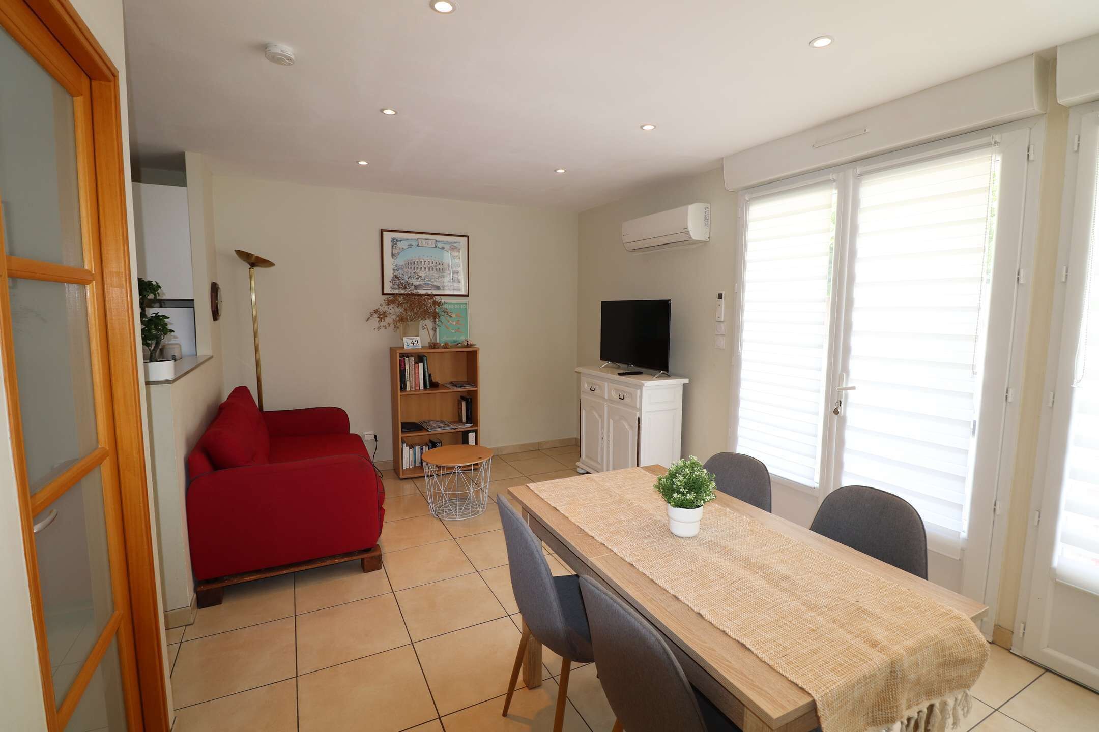 A dining area with a table, chairs, a red sofa, a bookshelf, and a television.