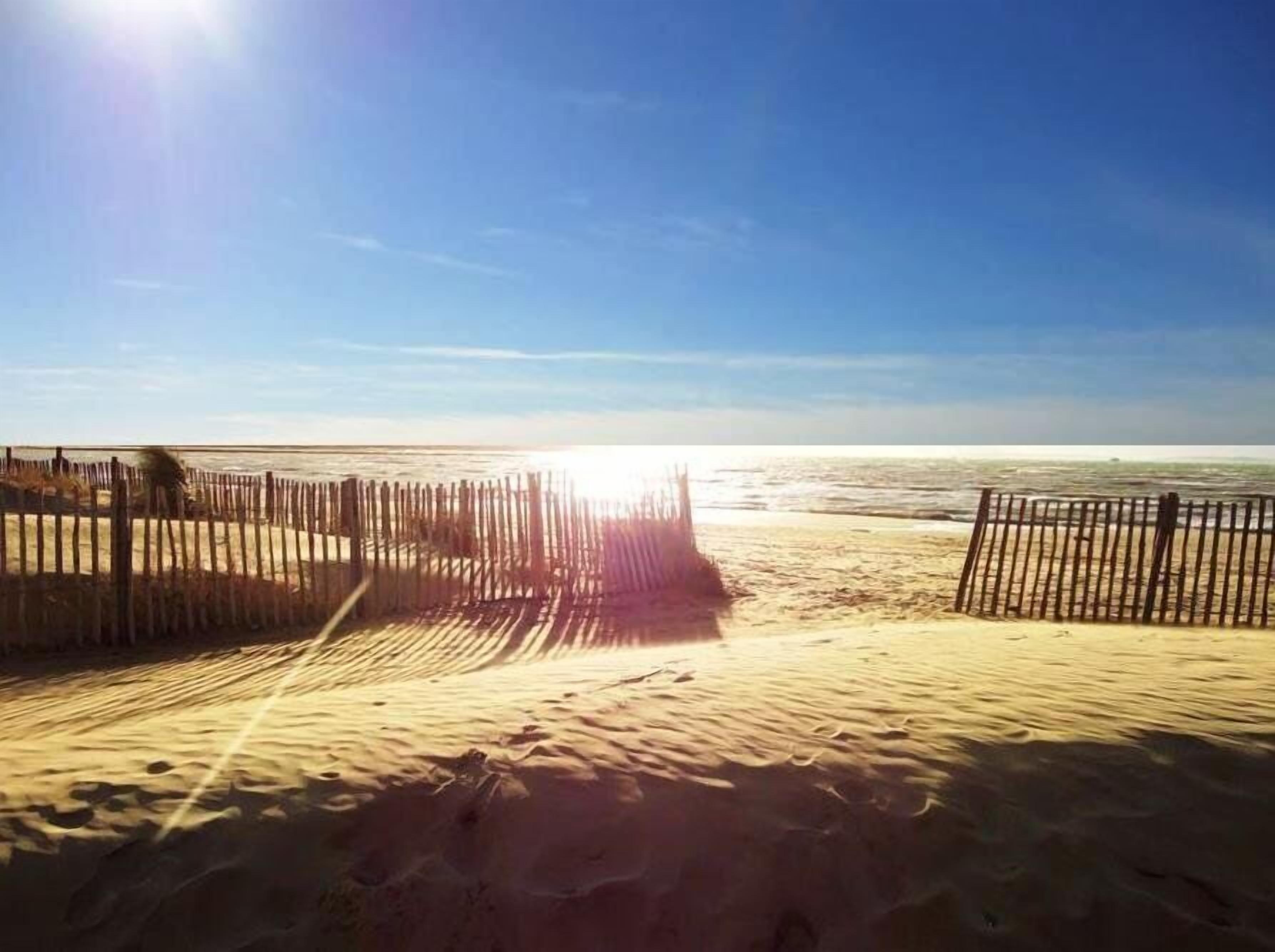 A sandy beach with a wooden fence and a clear sky.
