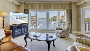 A living room with a television displaying 'Island Getaway Rentals', a large window with a view of boats and water, a ceiling fan, and a sofa.