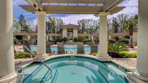 A pool area with a pergola, lounge chairs, and a building in the background.