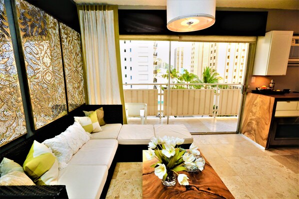 Una sala de estar moderna con un sofá, una mesa de centro con flores y vistas a un balcón con plantas.