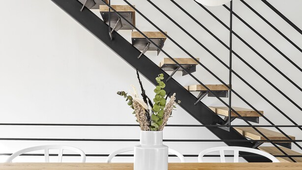 A modern interior with a wooden dining table, a potted plant, and a staircase with black railings and wooden steps. - Absolute Luxury! Sleeps 16! RoofDeck/Gym/Wet Bar (Philadelphia)