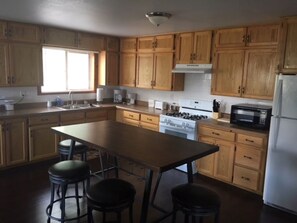 A kitchen with wooden cabinets, a central island with stools, a stove, a microwave, and a refrigerator. - The Golden Getaway, #A (Crestone)