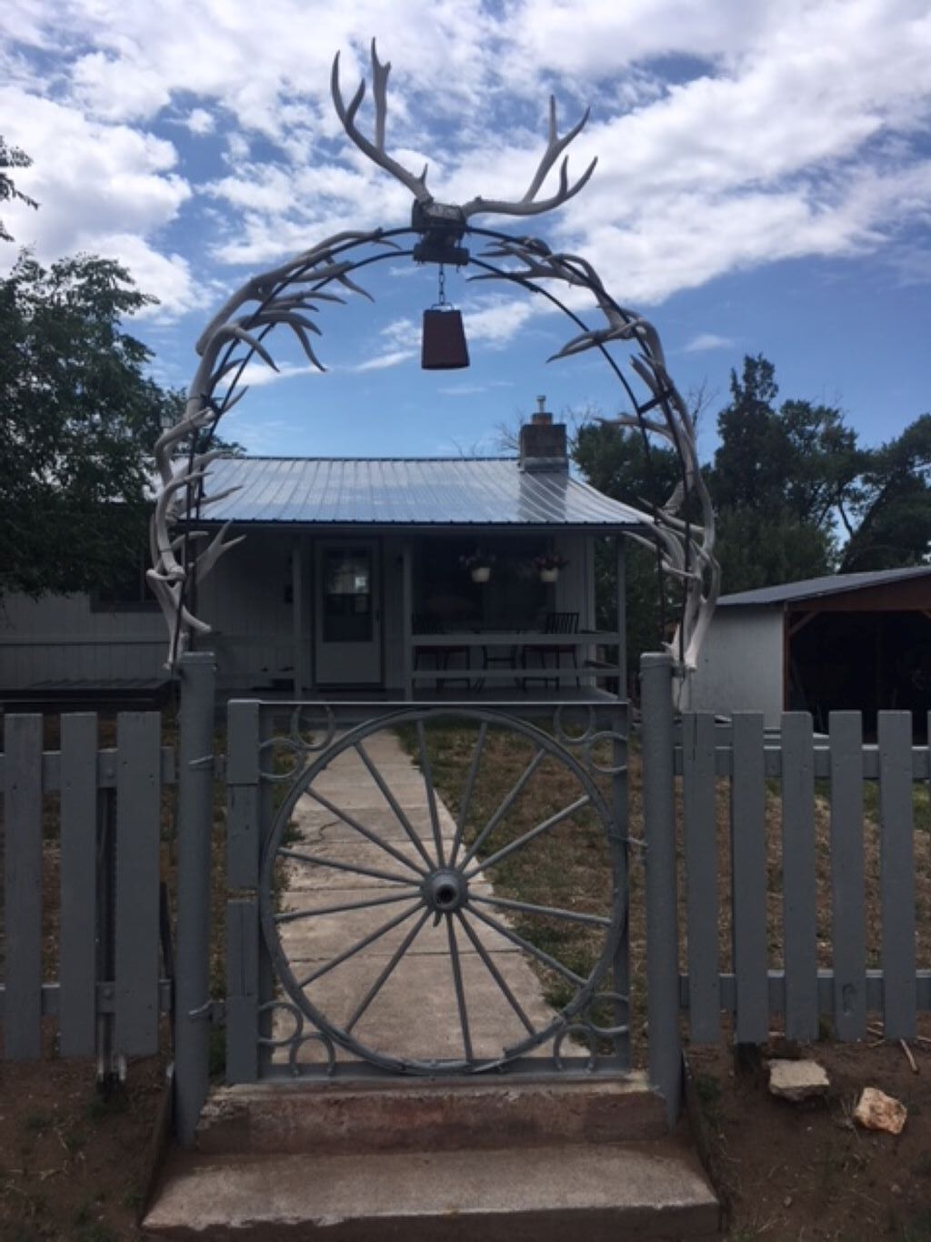 Une porte en métal avec une grande roue, une sculpture représentant la tête d’un cerf et une maison en arrière-plan.